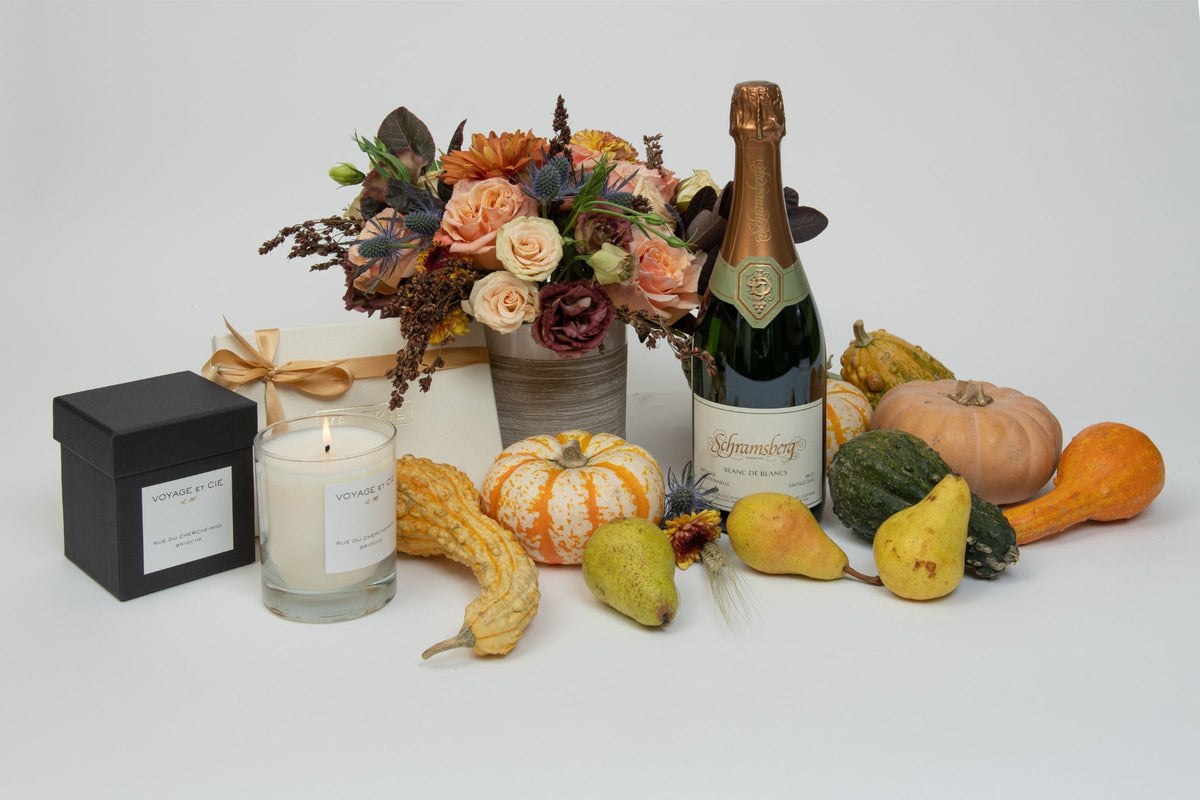 Fall flower arrangement with garden roses and dahlias styled as a hostess gift with a candle, sparkling wine, and pumpkins