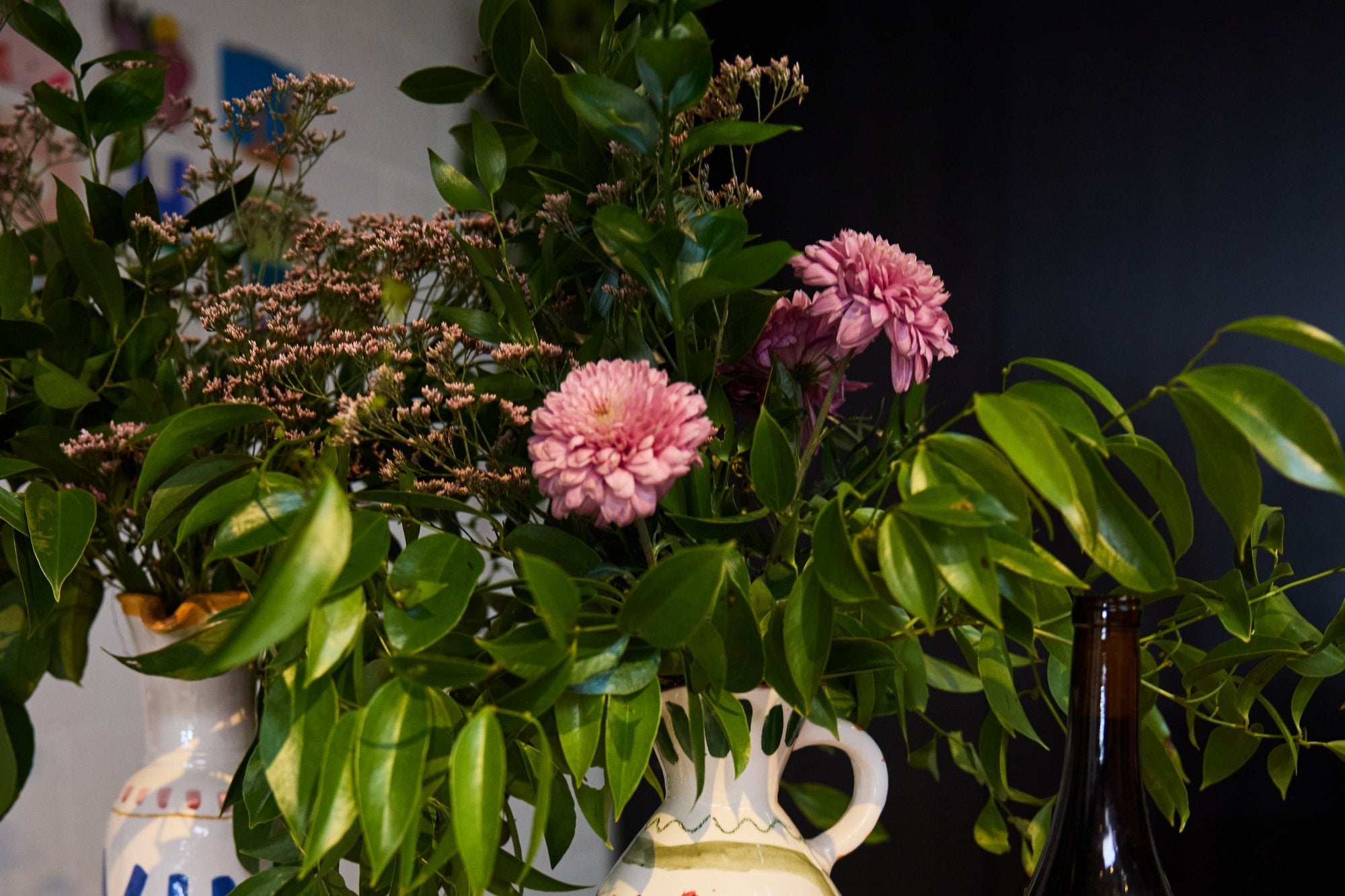 Late summer flower arrangement of pink dahlias and greenery in hand-painted ceramic pitchers on a styled table