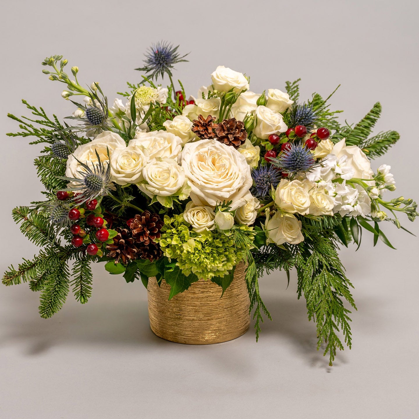 A flower arrangement featuring winter white flowers, pinecones, and seasonal winter greens. 